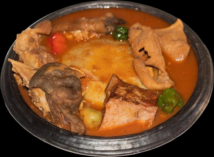 Fufu in light soup with assorted meat and peppers, in a black clay pot