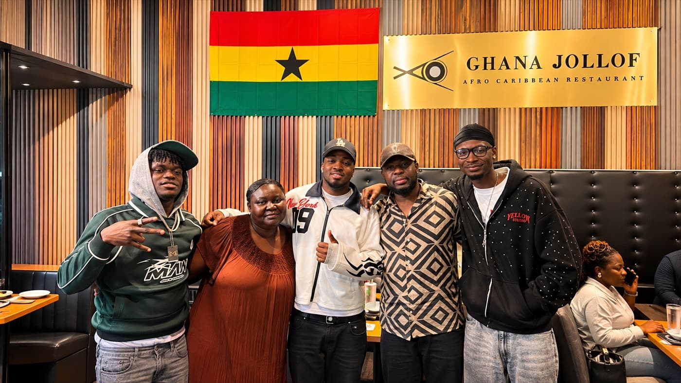 Guests in front of the Ghana flag and the Ghana Jollof Afro Caribbean Restaurant sign